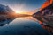 adrium Holz-Bild 120 x 80 cm: Wunderschöne Landschaft mit hohen Bergen mit beleuchteten Gipfeln, Steinen im Bergsee, Reflexion, blauem Himmel und gelbem (95513775)