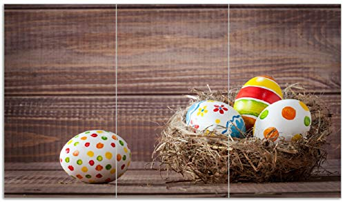 Wallario Herdabdeckplatte/Spritzschutz aus Glas, 3-teilig, 90x52cm mit 13mm hohen Füßen, für Ceran- und Induktionsherde, Bunte bemalte Eier an Ostern im Vorgelnest vor hölzerner Wand